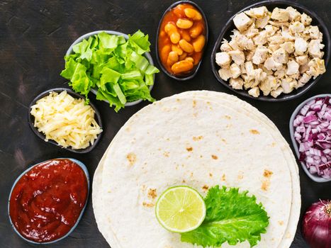 Traditional mexican tortilla with mix of ingredients on black concrete background