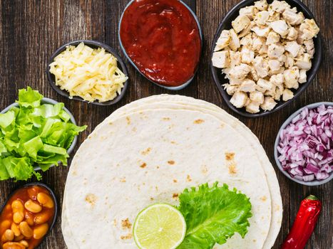 Traditional mexican tortilla with mix of ingredients on brown wooden background