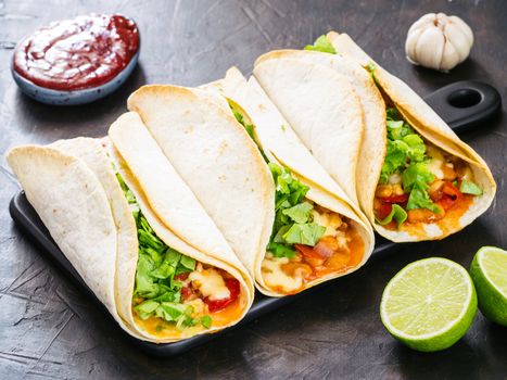 Three homemade tacos with chicken, vegetables and salsa. Latin food tacos on black wooden cutting board over black table