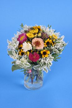 Bouquet of different wildflowers in a glass on a blue background