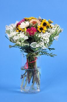 Bouquet of different wildflowers in a glass on a blue background