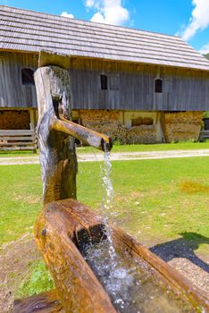 Traditional Wooden water trough, water well with trough in European Alps, Robanov kot, Slovenia, a farm shed in background