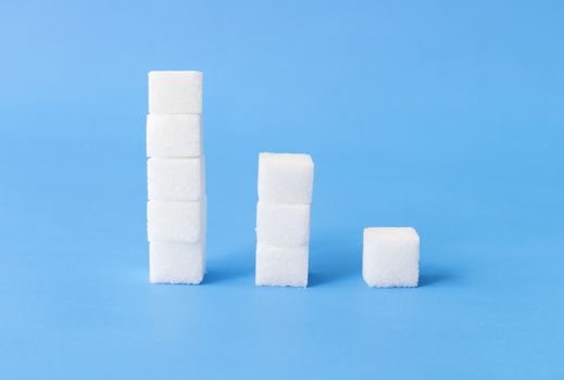 High to low stacks of sugar cubes with blue background, health care concept