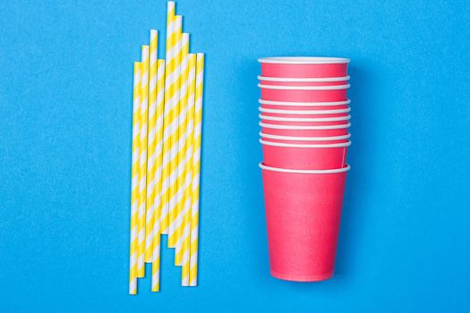 Colorful paper cups and striped straws for birthday party on the blue background