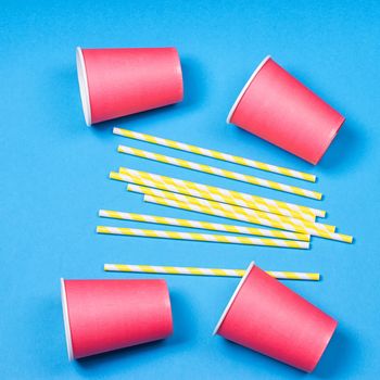 Colorful paper cups and striped straws for birthday party on the blue background