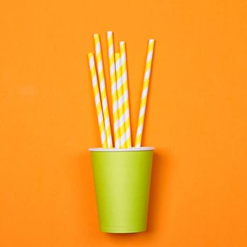 a bundle of multi-colored drinking straws in a paper Cup on a orange background. fashion minimal. flat lay