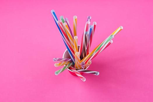 a bundle of multi-colored drinking straws in a paper Cup on a pink background. fashion minimal. flat lay