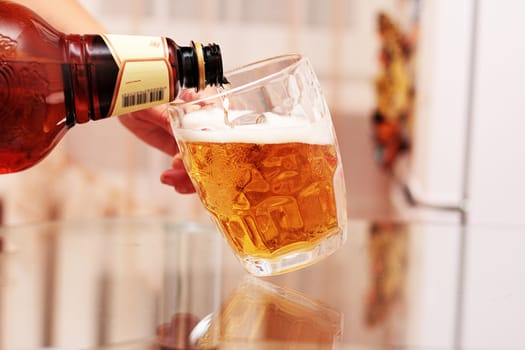 A woman pours beer into a glass mug from a plastic bottle.