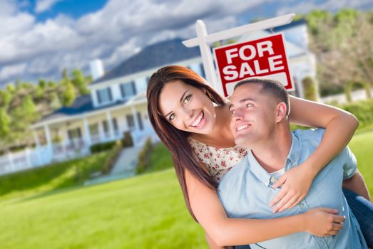 Playful Excited Military Couple In Front of Home with For Sale Real Estate Sign.