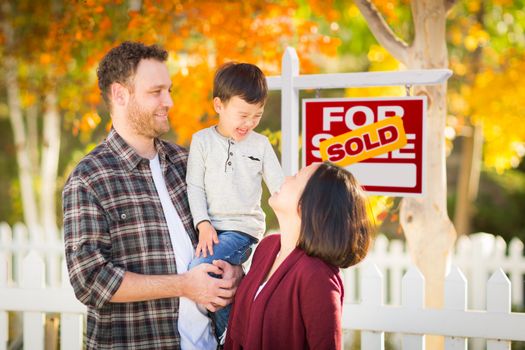 Young Mixed Race Chinese and Caucasian Family In Front of Sold For Sale Real Estate Sign and Fall Yard.