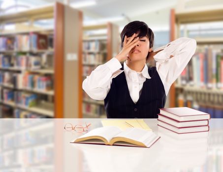 Young Female Mixed Race Student Stressed and Frustrated In Library with Blank Pad of Paper and Books.