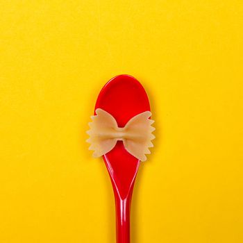 Farfalle bows pasta and red spoon on the yellow background