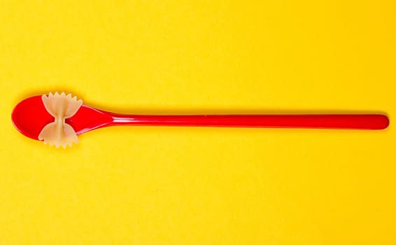 Farfalle bows pasta and red spoon on the yellow background