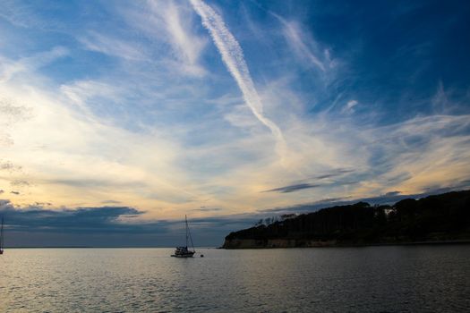 Beautiful sky with chemtrails from a plane in the nature above an ireland, a boat and the sea.