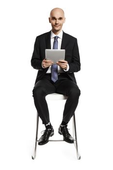 Studio shot of young businessman with digital tablet sitting on a chair.
