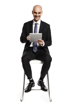 Cheerful young businessman sitting on a chair and looking at digital tablet. Isolated on white background.