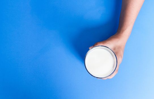 Hand holding glass of milk on blue background, food and drink for healthy concept