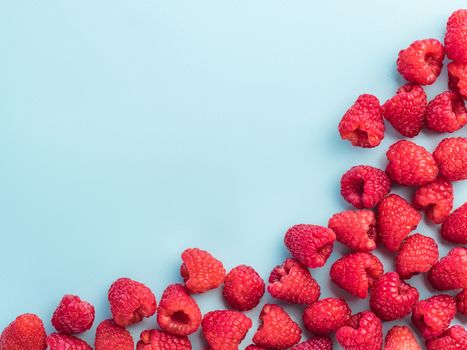 Background of raspberries. Raspberry on blue background with copy space. Isolated one edge. Summer and healthy food concept, Top view or flat lay.