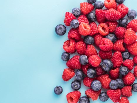 Background of raspberries and blueberries. Raspberry and blueberry on blue background with copy space. Summer and healthy food concept, Top view or flat lay.