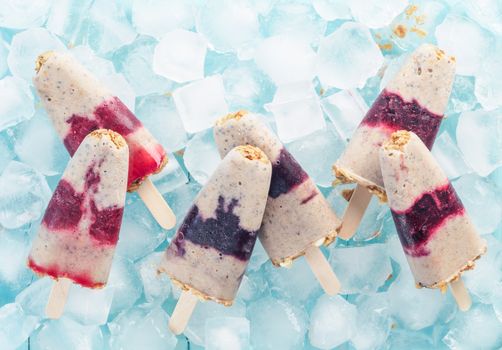 Homemade ice cream popsicle with berries, granola and chia seeds. Healthy summer breakfast concept. Popsicles from yogurt and banana with berries and granola. Top view. Copyspace