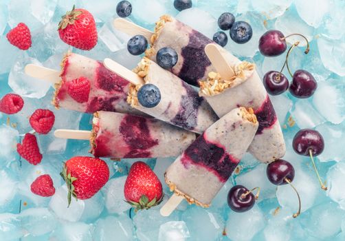 Homemade popsicle and cherry, blueberry, strawberry, raspberry. Healthy summer breakfast concept. Popsicles from yogurt and banana with berries, granola and chia seeds. Top view.