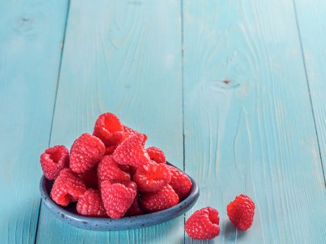 Fresh raspberries on blue wooden background. Raspberry in blue trandy plate. Summer and healthy food concept. Copy space.