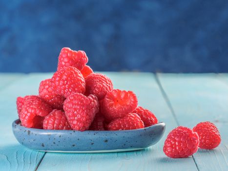 Fresh raspberries on blue wooden background. Raspberry in blue trandy plate. Summer and healthy food concept. Copy space.
