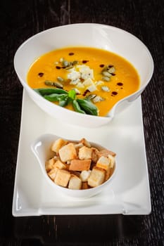 Pumpkin soup with cream and pumpkin seeds on dark wooden background. Copy space.