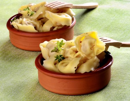 Delicious Meat Cappelletti with Herbs in Ceramic Bowls with Wooden Forks closeup on Green Napkin background