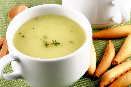 Delicious Cream Asparagus Soup in White Soup Cup with Bread Sticks and Wooden Spoon closeup on Green Napkin