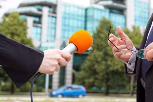 Female reporter holding microphone interviewing business person or politician
