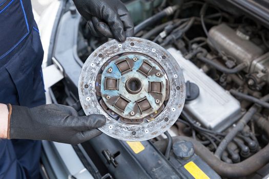 Auto mechanic wearing protective work gloves holding old clutch disc over a car engine