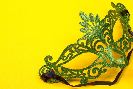 Green, mardi gras mask on a bright yellow background