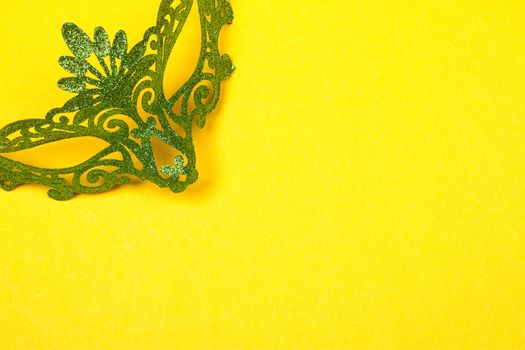 Green, mardi gras mask on a bright yellow background