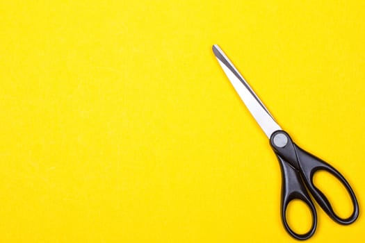 Black stationery scissors on a yellow background