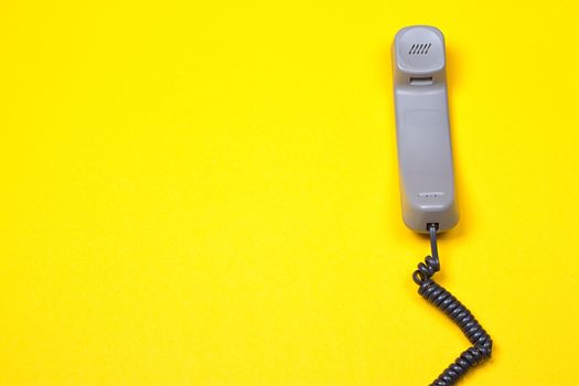 Top view of gray telephone handset. receiver and cord on yellow background.