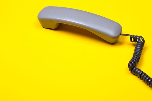 Top view of gray telephone handset. receiver and cord on yellow background.