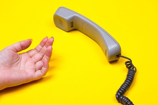 female hand lies next to the telephone receiver on the wire on a yellow background