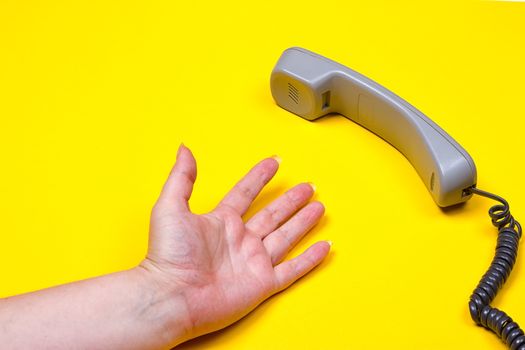 female hand lies next to the telephone receiver on the wire on a yellow background