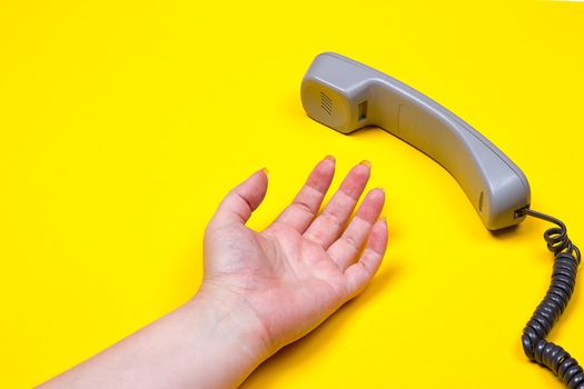 female hand lies next to the telephone receiver on the wire on a yellow background