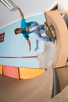 Skateboarder performing a backside turn on mini ramp at indoor skate park.