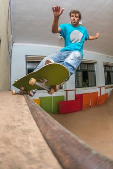Skateboarder performing a frontside pivot grind on mini ramp at indoor skate park.