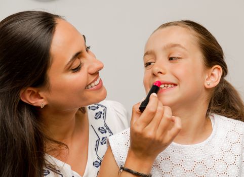 Mother playing with her daughter applying lipstick