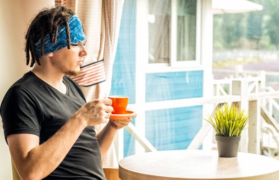 a man with dreadlocks is drinking tea looking to the window