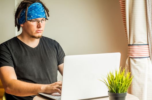 a young caucasianman with dreadlocks is working on the computer at home