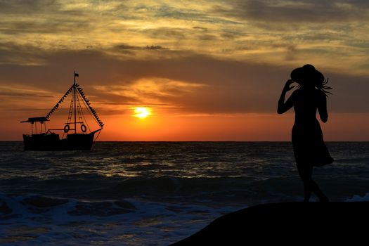 Back view of woman silhouette watching a sail boat at sunrise