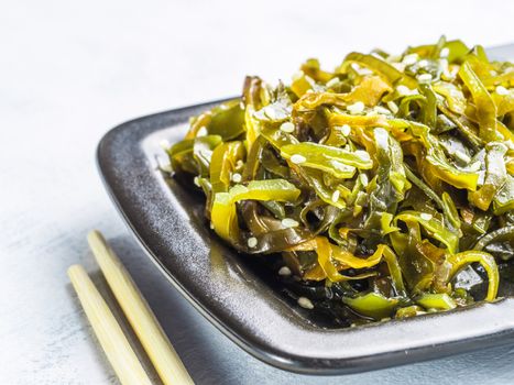 Close up view of kelp seaweed salad with sesame seeds in black plate on gray concrete background. Copy space.