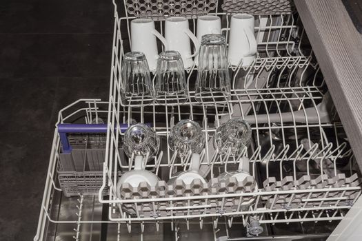 View from above on an open dishwasher with clean cup, glasses and plates.