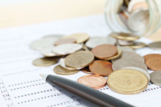 Business, finance, savings or loan concept : Coins scattered from glass jar and pen on saving account passbook or financial statement