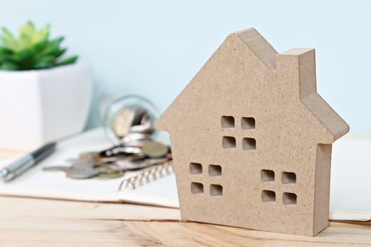 Business, finance, savings, property ladder or mortgage loan concept : Wood house model in front of coins scattered from glass jar